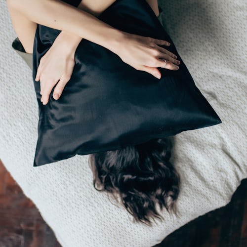 Portrait of young beautiful woman hugging a pillow while lying on her bed at home.