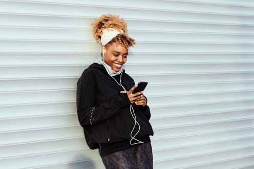 Beautiful African-American Woman leaning on the white garage door using her phone for texting. She i...