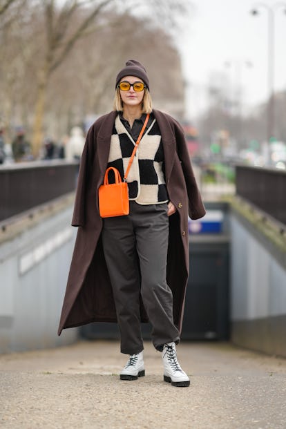PARIS, FRANCE - JANUARY 25: A guest wears gold earrings, a brown ribbed wool beanie, orange sunglass...