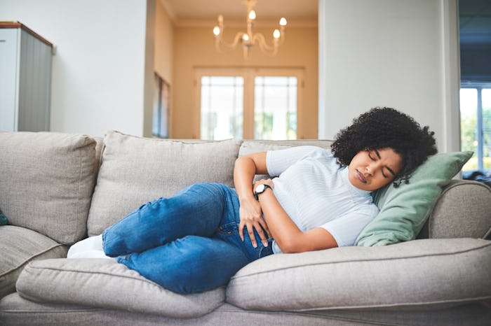 Woman lying down on sofa in discomfort