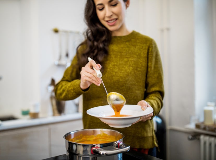 Young woman serving squash soup in bowl at kitchen during dinner party