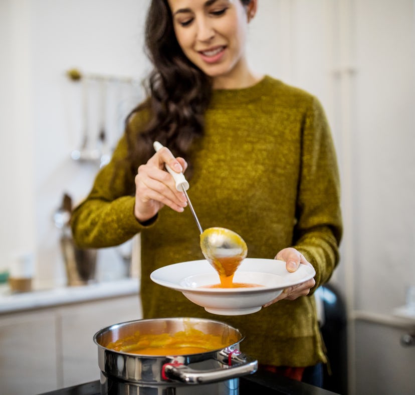 Young woman serving squash soup in bowl at kitchen during dinner party