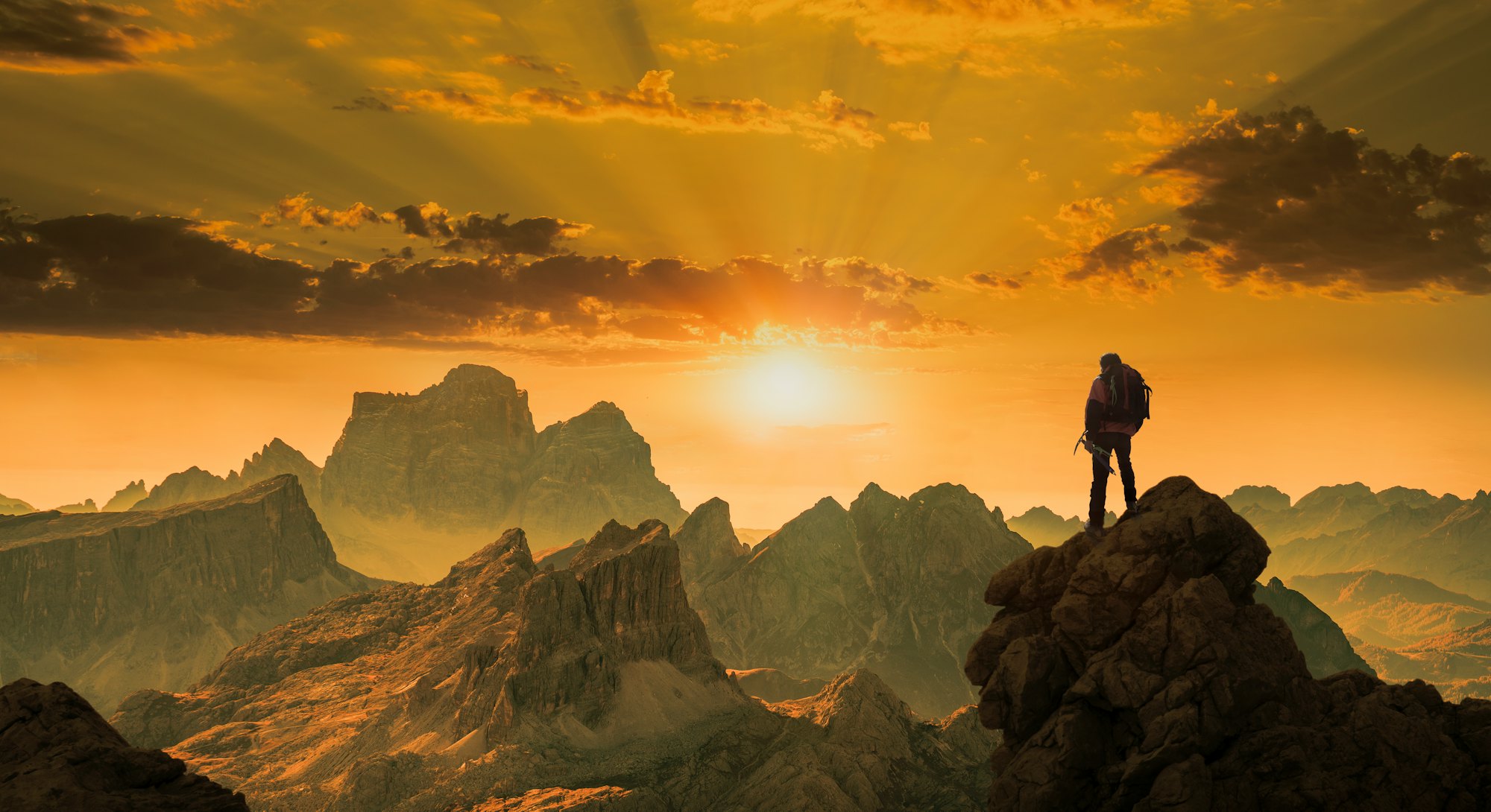 Rear view of a senior caucasian climber standing on a rock and watching a spectacular sunset over ro...