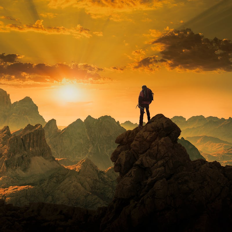 Rear view of a senior caucasian climber standing on a rock and watching a spectacular sunset over ro...