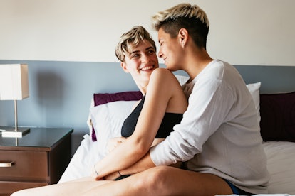A lesbian couple cuddles in bed. Past life connections in astrology show up through comparing birth ...