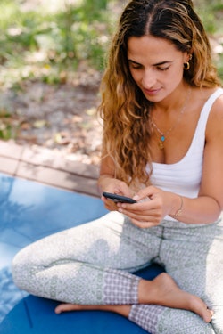 A woman on a yoga mat consults a habit-tracking app on her iphone. These are the best goal apps for ...