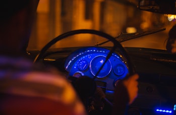 A view from behind of an unrecognizable taxi driver as he pilots his old American car through the st...