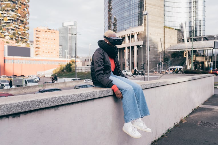 Italy, Woman withVRgoggles sitting on wall in city