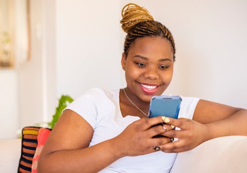 Close-up of a smiling young woman sitting on sofa using a smart phone at home