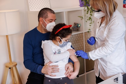 Girl sitting in father's lap and receiving coronavirus vaccine in doctor's office