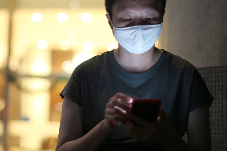 A woman with a white mask over her mouth is using her smartphone.