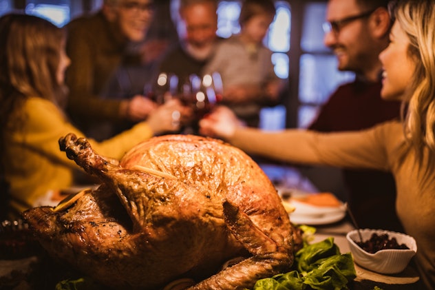 Close up of Thanksgiving stuffed turkey on dining table with family toasting in the background. than...
