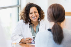 A smiling mid adult female doctor listens as a female patient discusses her health in an article abo...