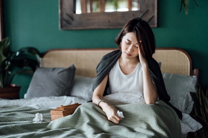 Young woman feeling sick and suffering from a headache, sitting on the bed and taking a rest at home