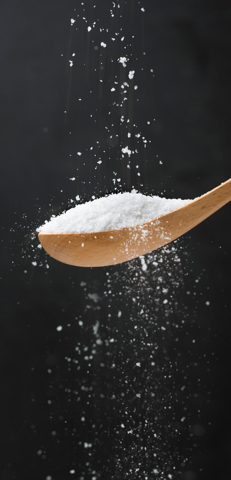 Salt flowing into a wooden spoon on black background. Close up image.