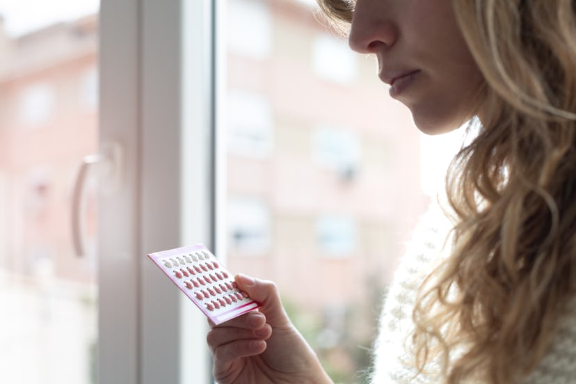 Close up of young woman holding contraceptive pills at home in an article about how long does birth ...