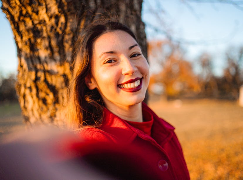 Young woman takes a selfie in a red coat as she thinks about her October 24, 2022 weekly horoscope.