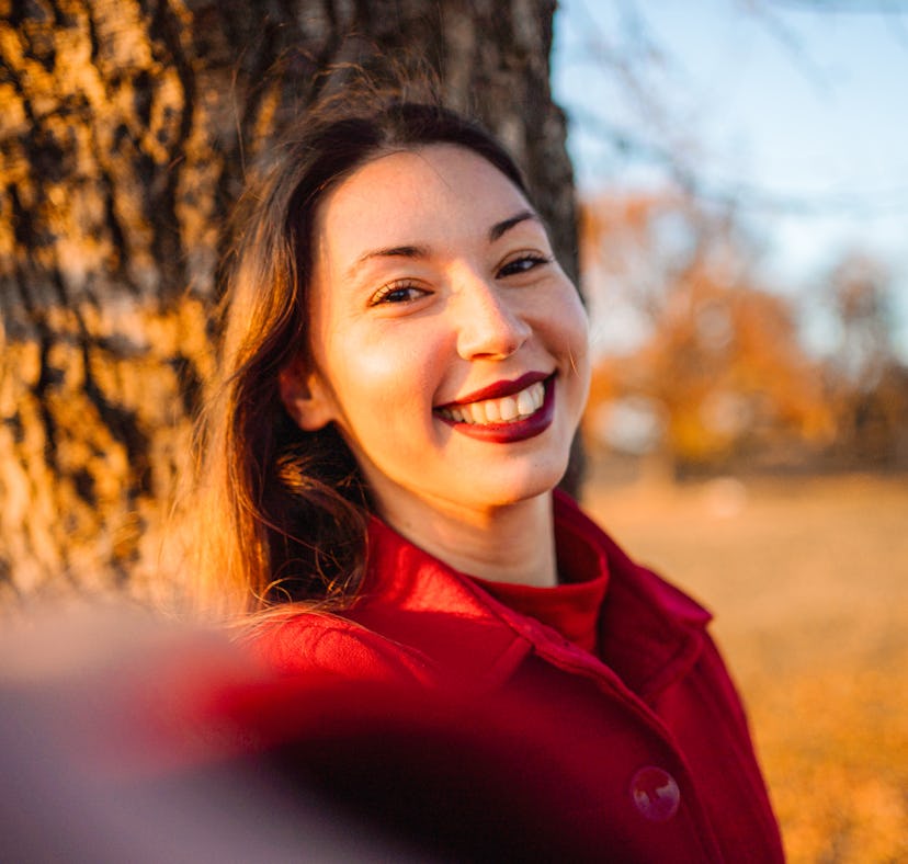 Young woman takes a selfie in a red coat as she thinks about her October 24, 2022 weekly horoscope.