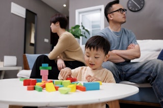 This is an Asian family. The little boy is playing with building blocks on the table and his parents...