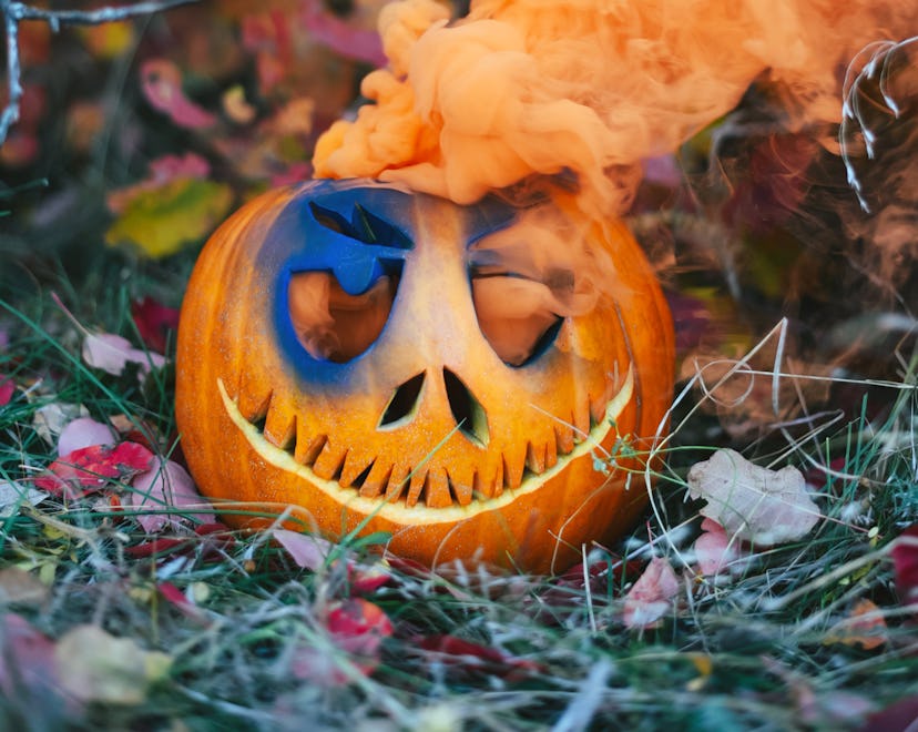 Halloween pumpkin with a skeleton face carving with orange smoke billowing from the top, a jack-o'-l...