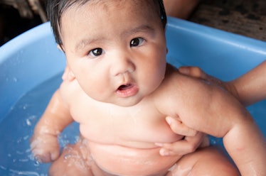 A naked chubby baby getting a bath.