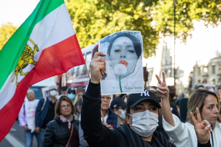 Protesters holding Iranian flags and images of Mahsa Amini and with hands daubed with fake blood mar...