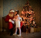 一个孩子站在圣诞老人旁边，背景是一棵圣诞树。
