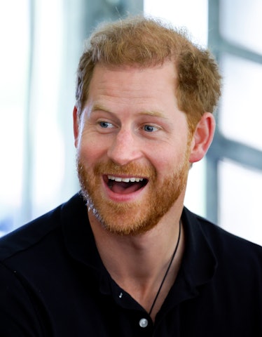 Prince Harry smiles off-camera; he is alone in the image in a black button up