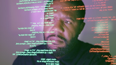 Stock image,   close up of a man’s face looking through a clear screen displaying computer code (pyt...