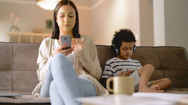 Cropped shot of an attractive young mother sitting and using her cellphone while her son plays video...
