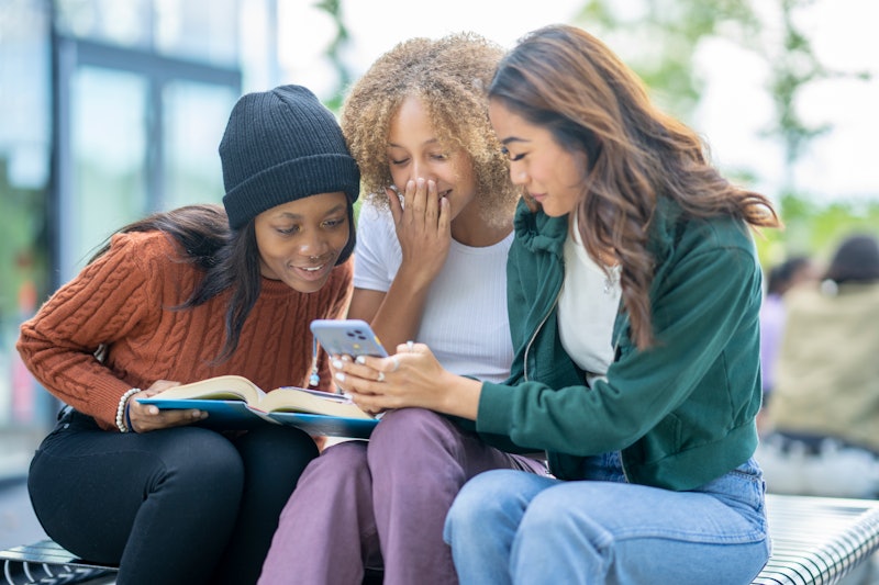 A small group of three University students sit outside on campus as they catch up on social media wi...