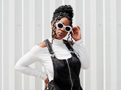 Young woman in denim overalls poses wearing white glasses as she thinks about how every sign will be...