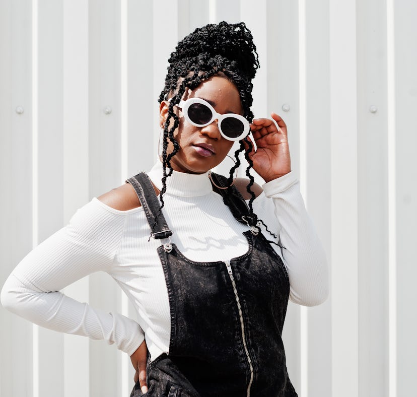 Young woman in denim overalls poses wearing white glasses as she thinks about how every sign will be...