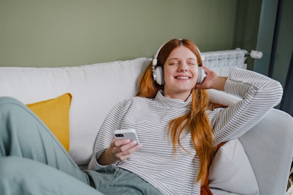 young woman relaxes on couch and listens to music through headphones as she thinks about her october...