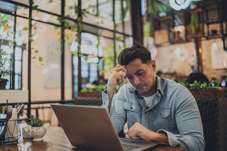 Worried mid adult businessman using laptop in a coffee shop