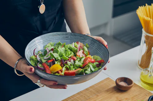 A young adult woman in the kitchen, holding a healthy vegan salad, close up