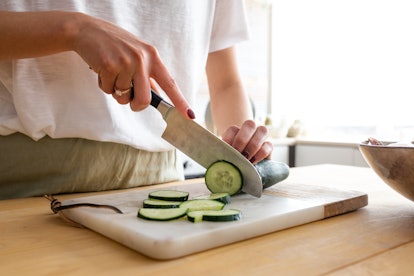 Close up image of unrecognisable woman cutting cucumber on a chopping board to cook meal. Making a h...