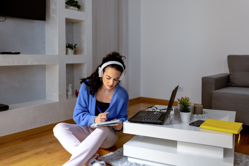 Beautiful hardworking businesswoman with headphones educating herself at home using internet and wri...