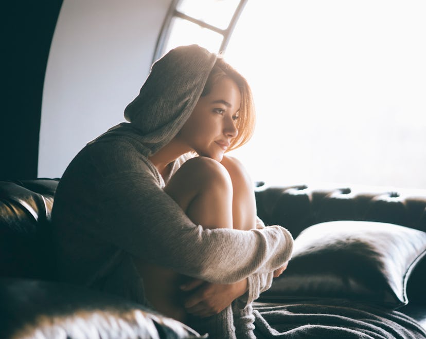 A women with knees pulled into her chest, on a couch, staring into the distance, in an article about...