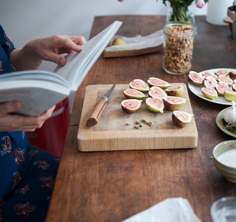 Woman reading a cookbook on how to make caramelized figs for a salad for a group of people.