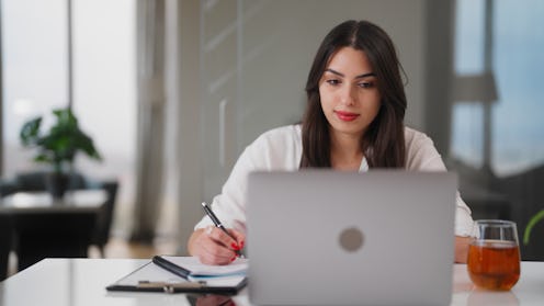 A young woman is sitting at table and using a laptop at home.