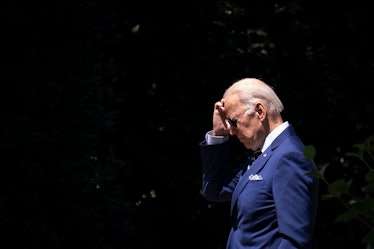Joe Biden is walking outside, wearing aviator sunglasses and a navy blue suit