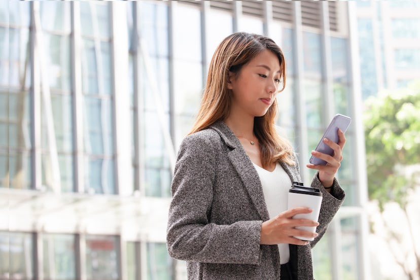 A young office lady is checking  email who is holding a cup of  coffee