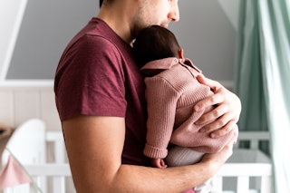 Father carrying his newborn daughter in the baby's room, with a white crib in the background. New ev...