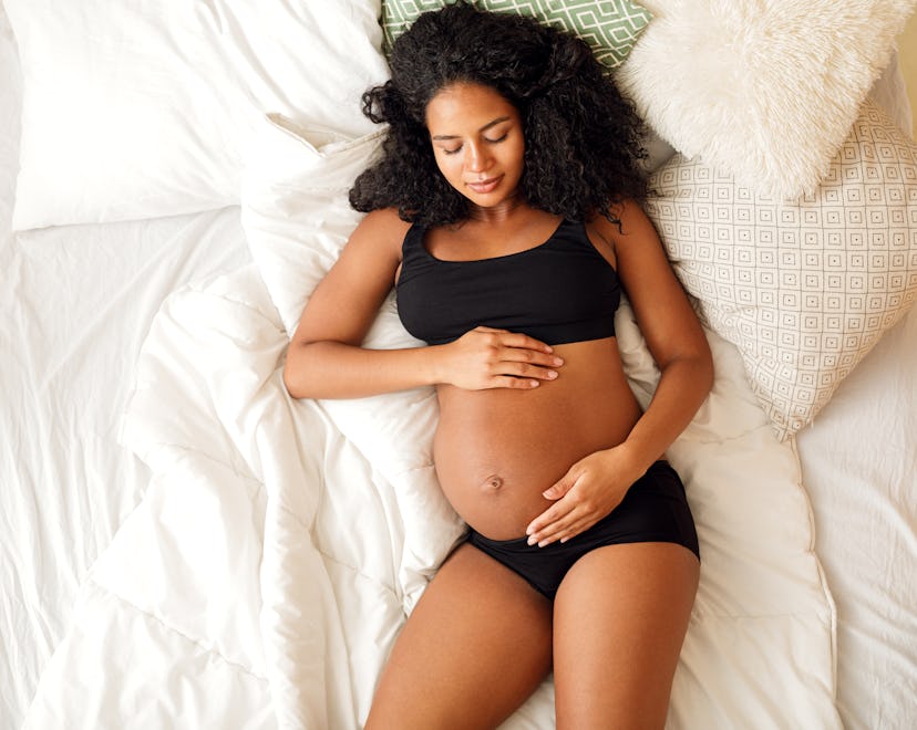 happy pregnant woman in black bra and panties lying on bed, what to avoid after losing mucus plug