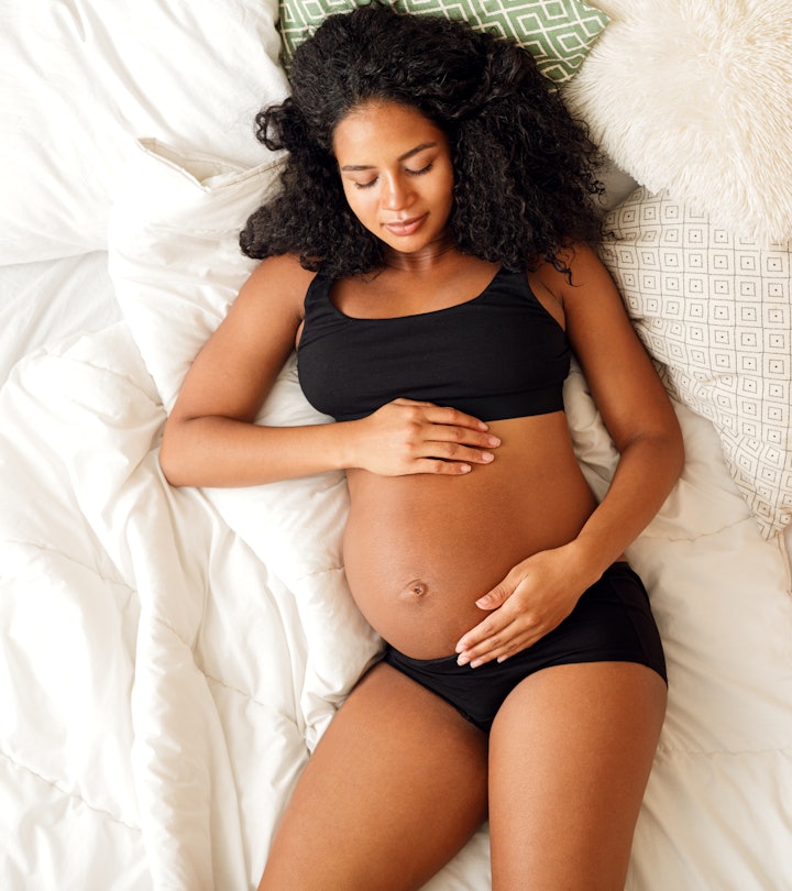happy pregnant woman in black bra and panties lying on bed, what to avoid after losing mucus plug