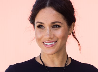 Meghan Markle smiling and posing with soft feminine makeup and hair styled in a messy bun