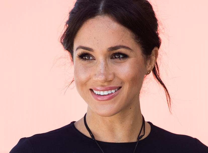 Meghan Markle smiling and posing with soft feminine makeup and hair styled in a messy bun