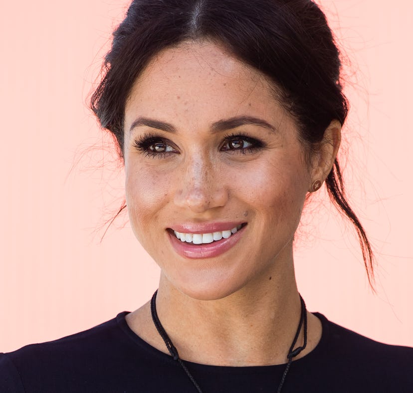 Meghan Markle smiling and posing with soft feminine makeup and hair styled in a messy bun