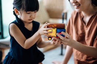 Cropped shot of young Asian mother and little daughter relaxing on carpet at home and playing with m...